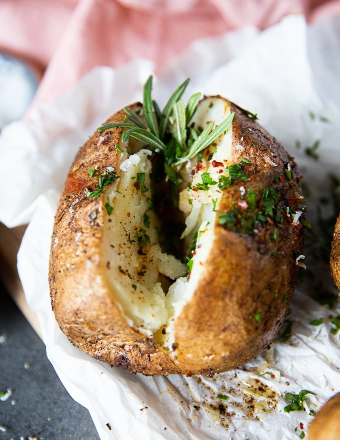 Close up of air fryer baked potato sliced and seasoned with a sprig of rosemary