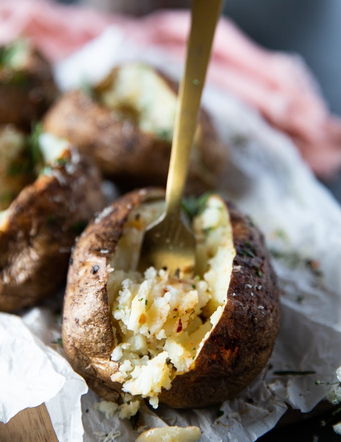 ready air fryer baked potato with butter, herb and spice on the inside and a fork trying to scoop out