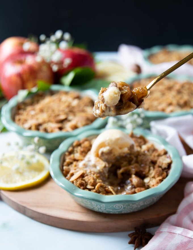 A spoon holding a piece of apple crumble and vanilla ice cream showing the saucy inside of the crumble