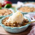 Apple crumble on a baking dish topped with vanilla ice cream and a spoon inside