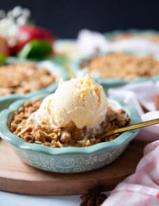 Apple crumble on a baking dish topped with vanilla ice cream and a spoon inside