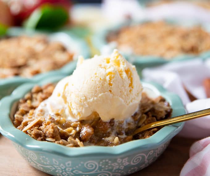 Apple crumble on a baking dish topped with vanilla ice cream and a spoon inside