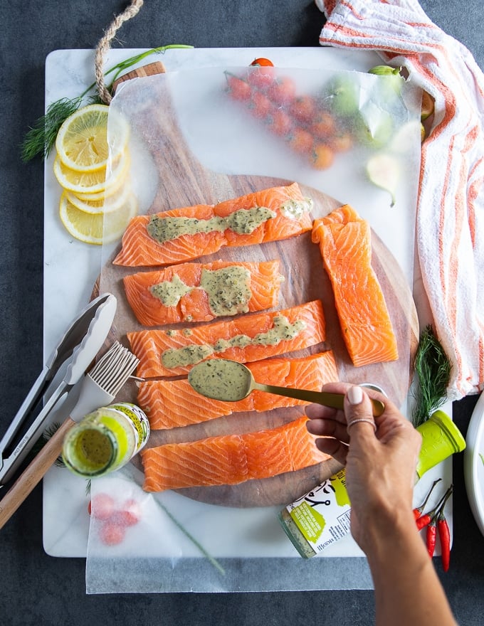 A hand drizzling the grilled salmon marinade over pieces of salmon fillets on a white marble 