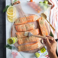 A hand brushing the salmon fillets with the grilled salmon marinade coating it well on both sides