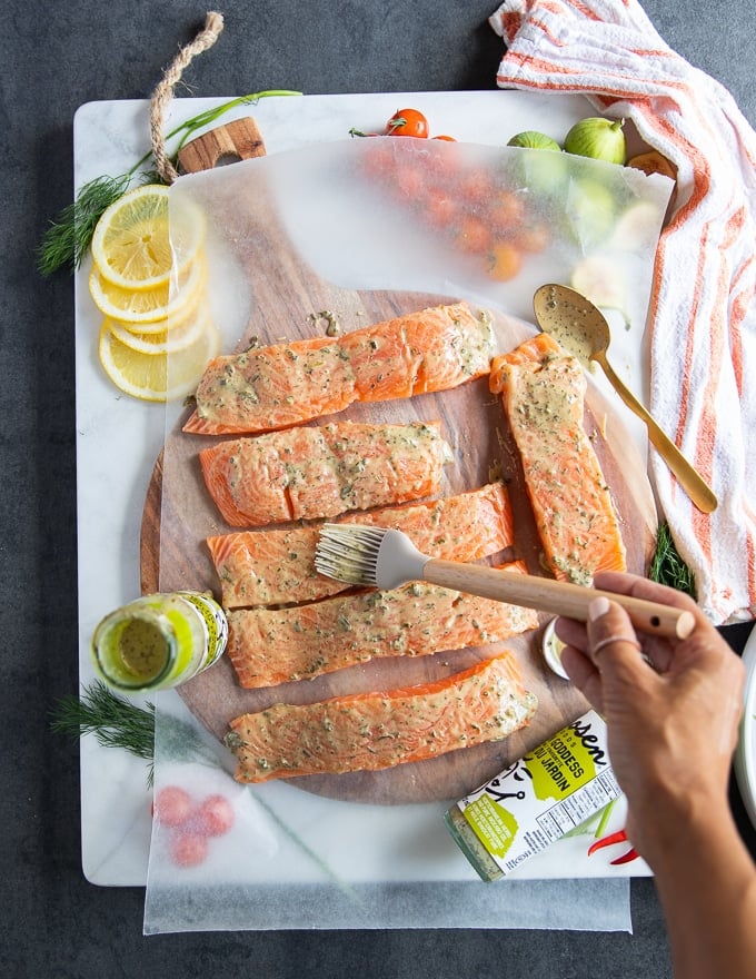 A hand brushing the salmon fillets with the grilled salmon marinade coating it well on both sides