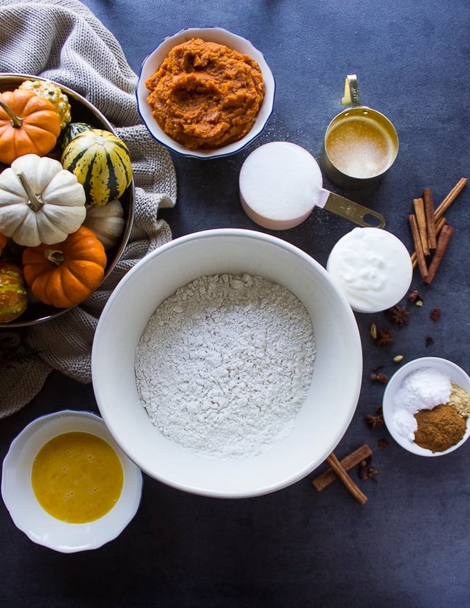 ingredients to make pumpkin donuts including flour, pumpkin, eggs, yogurt, oil, sugar, cinnamon and melted butter 