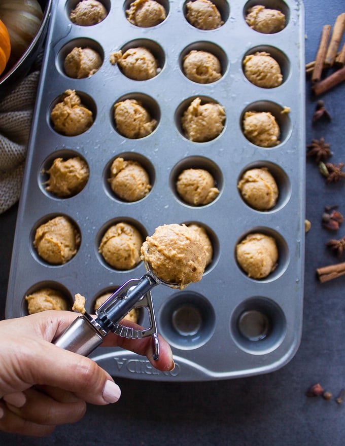 a hand holding an ice cream scoop showing how to scoop the batter into the prepared mini muffin tin for baking the donut holes