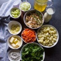 Ingredients for the chicken and gnocchi soup in small bowls including the gnocchi, rotisserie chicken, spinach, gnocchi, butter, stock, butter, onions, celery, carrots, flour and cream