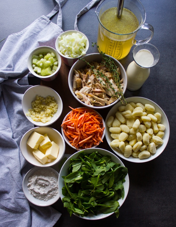 Ingredients for the chicken and gnocchi soup in small bowls including the gnocchi, rotisserie chicken, spinach, gnocchi, butter, stock, butter, onions, celery, carrots, flour and cream