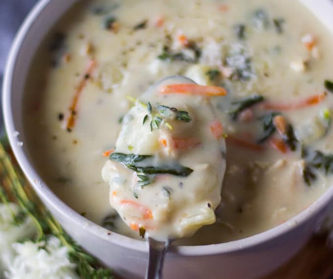 A bowl of chicken and gnocchi soup and a spoon scooping out some soup to show the texture