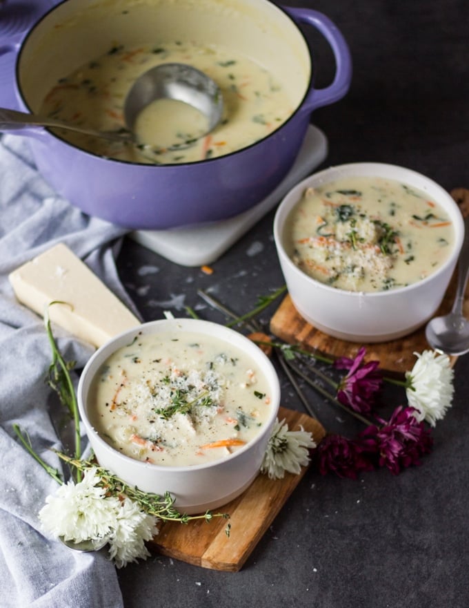 a large pot of soup in the background and two bowls of chicken and gnocchi soup recipe served and garnished with parmesan cheese on a wooden board
