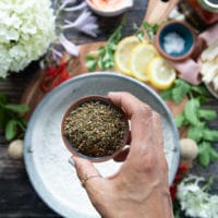 a hand holding a small bowl of zaatar spice and adding it to a bowl of flour to season the flour