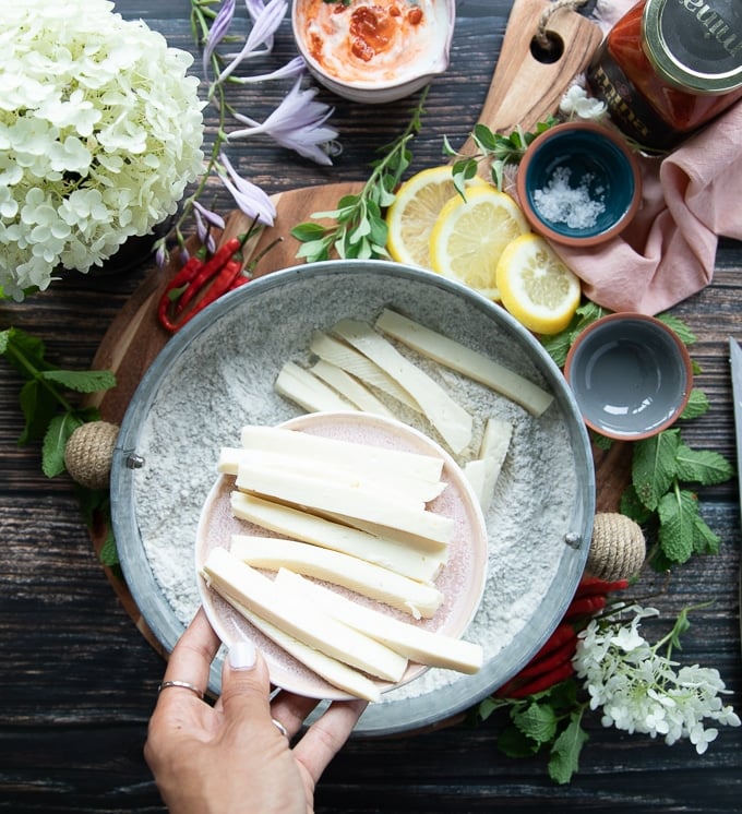 A hand pouring the sliced halloumi cheese into the flour bowl