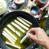 A hand adding the halloumi cheese into the frying pan