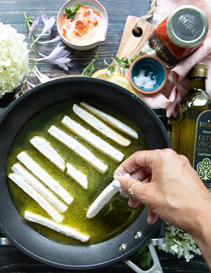 A hand adding the halloumi cheese into the frying pan