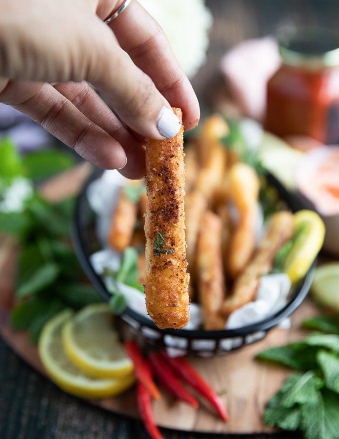 A hand holding one crispy halloumi fries to show how crispy and golden it is