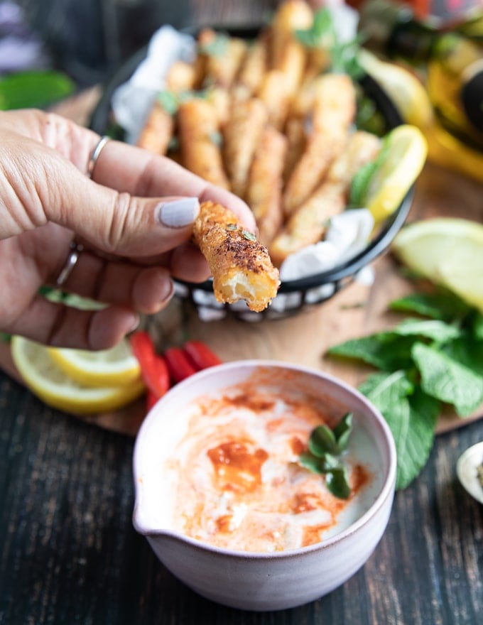 A hand holding a halloumi fries bitten to show the texture of the fried cheese and the sauce