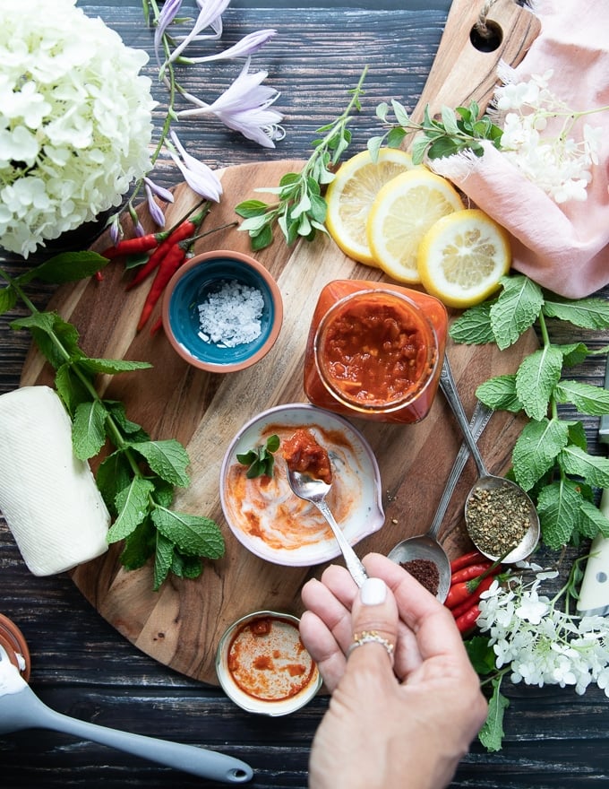 A hand mixing the yogurt harissa sauce in a bowl