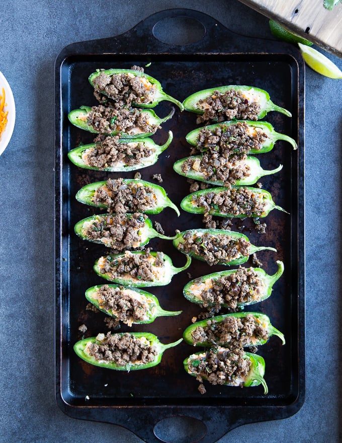 Jalapeño peppers on a baking sheet stuffed with the cheese mixture and topped with the spice lamb