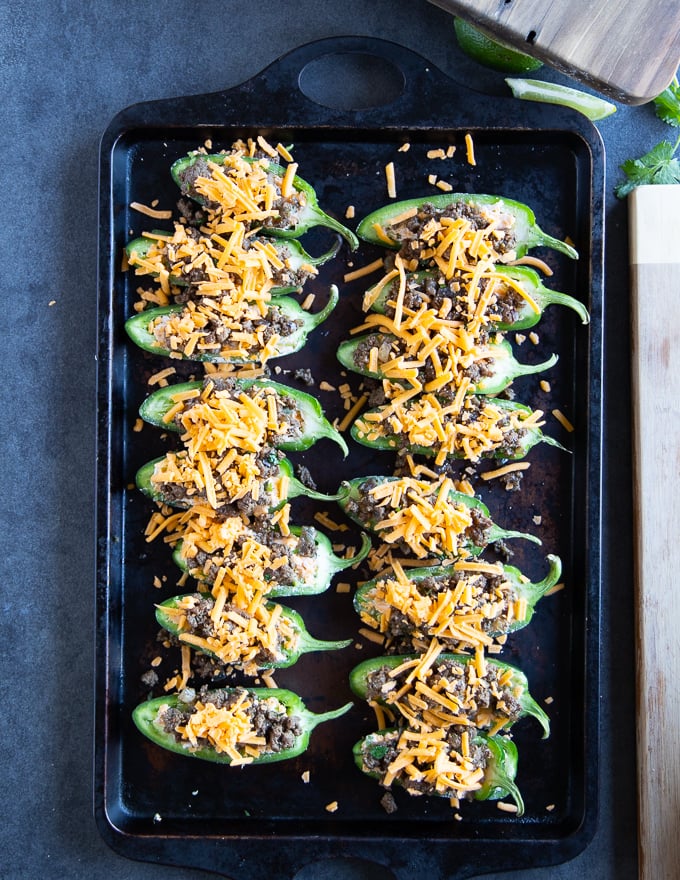 A final sprinkle of cheese is added over the stuffed jalapenos before going into the oven