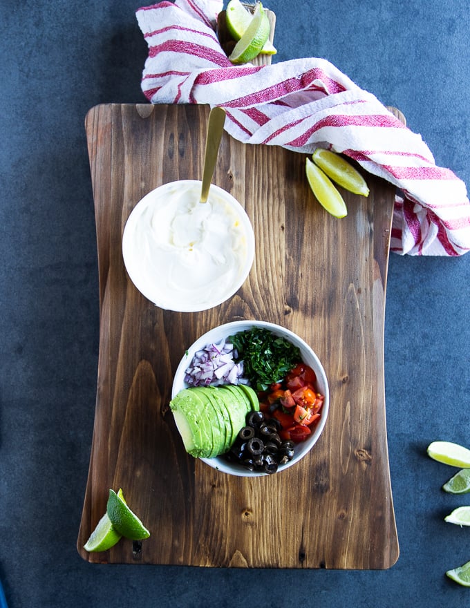 A colecyion of different nachos topping to sprinkle of the baked jalapenos including black olives, tomatoes, cilantro, onions, avocado and sour cream 