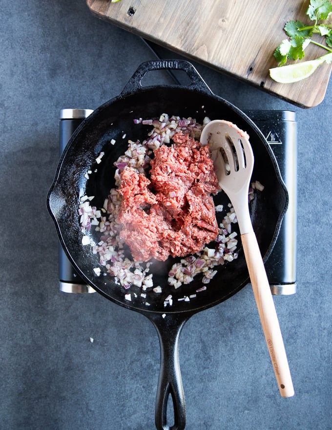 ground lamb cooking in a cast iron skillet with onions