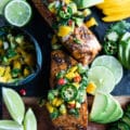 Air fryer Salmon on a wooden board surrounded by lime wedges, jalapenos, mango salsa
