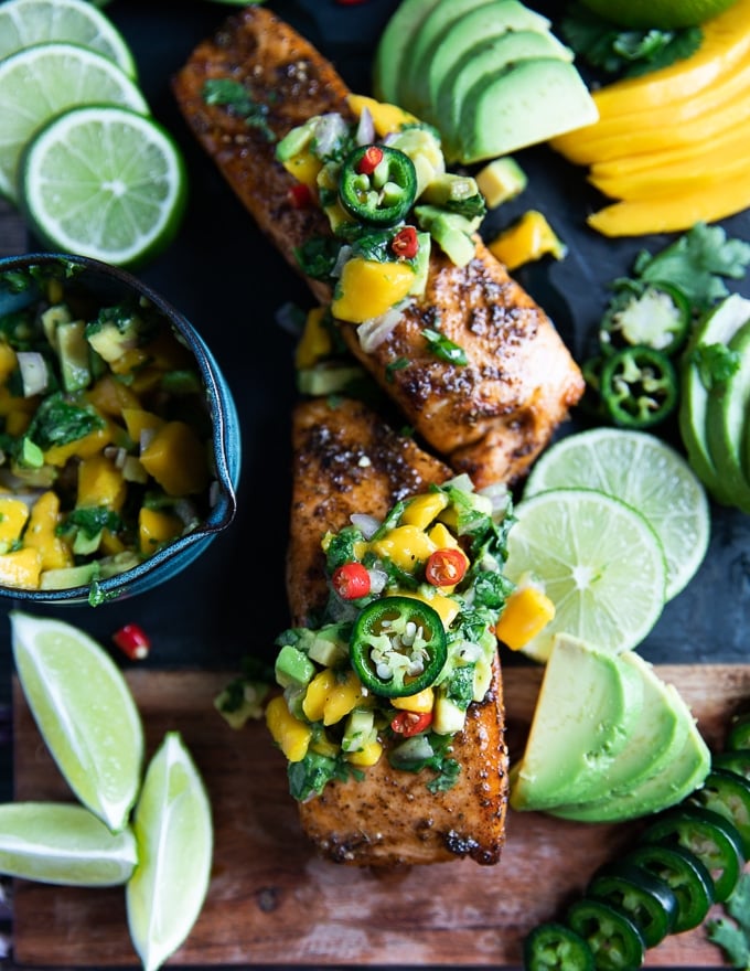 Air fryer Salmon on a wooden board surrounded by lime wedges, jalapenos, mango salsa 