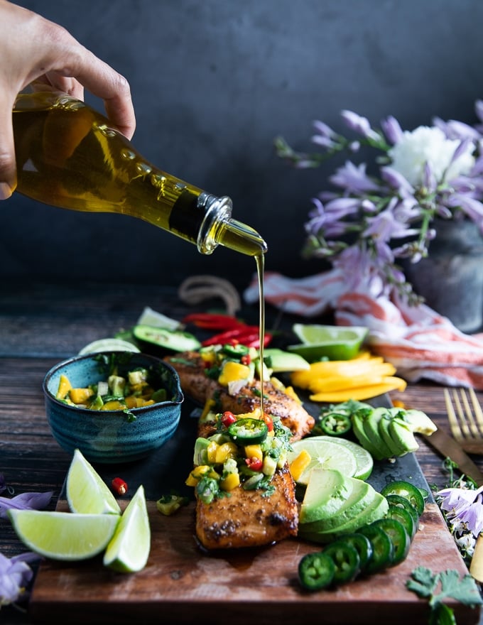 a hand pouring olive oil over the air fryer salmon for a finishing touch