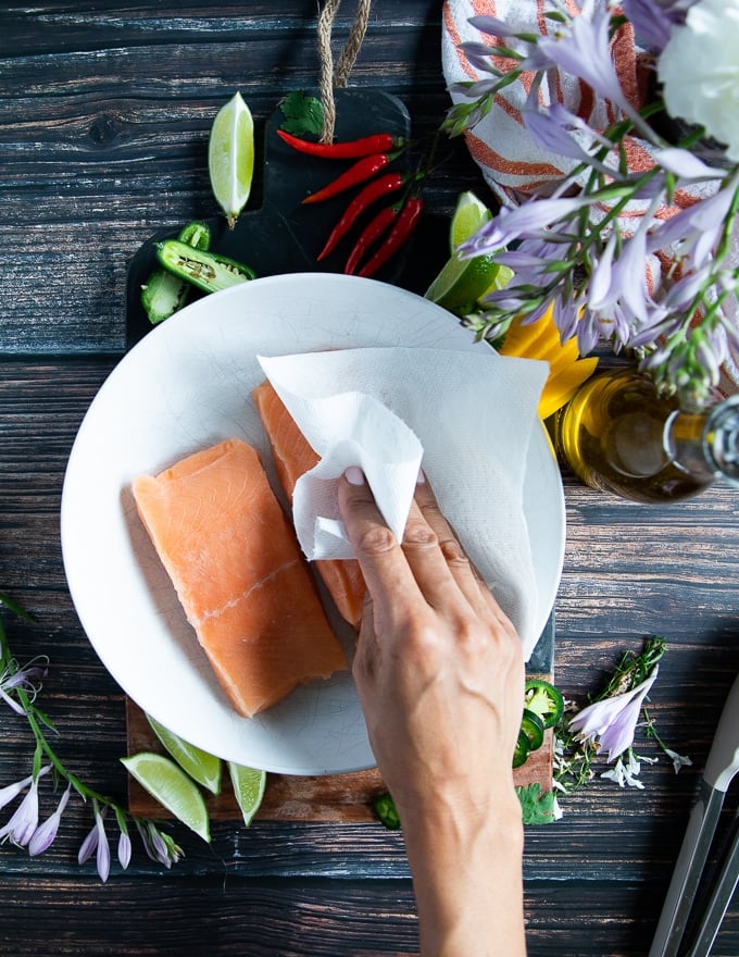 a hand patting down the salmon fillets with a paper towel before seasoning 