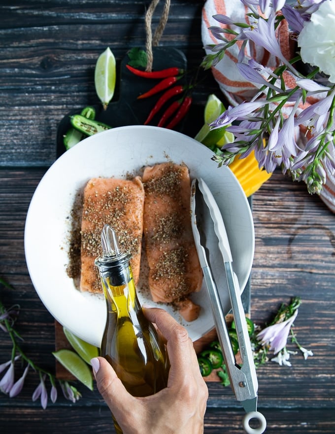 olive oil being poured over the seasoned salmon fillets for a crisp salmon in the air fryer 