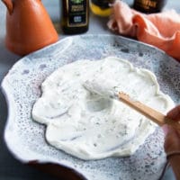 A hand spreading the yogurt sauce over the serving plate