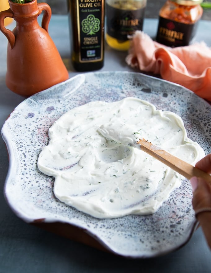 A hand spreading the yogurt sauce over the serving plate