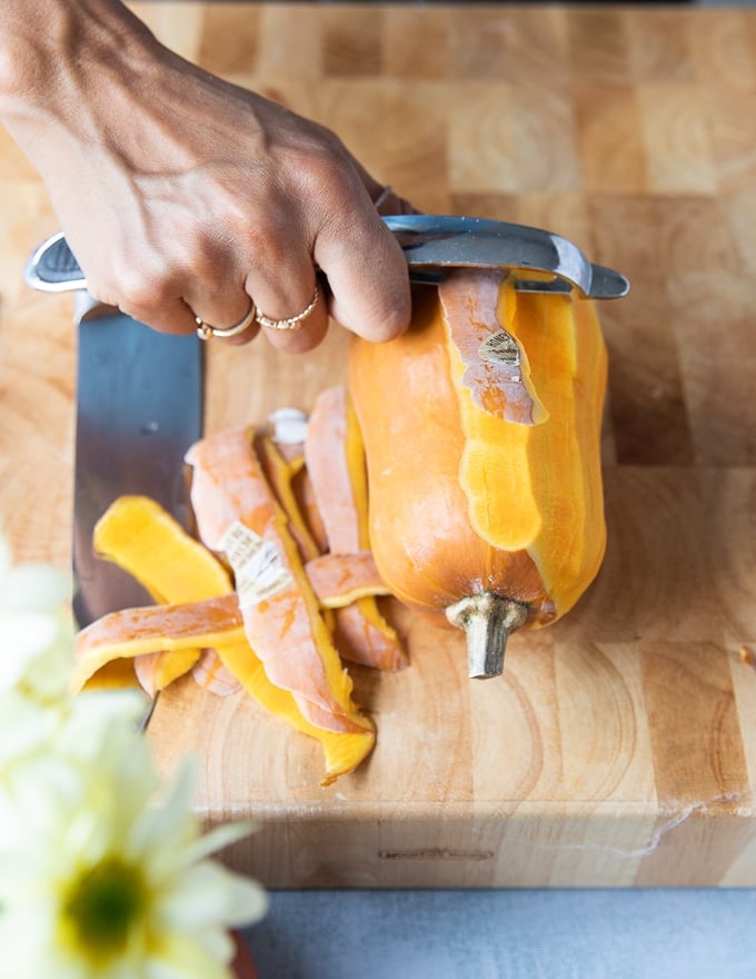 A hand peeling off the skin from the honeynut squash