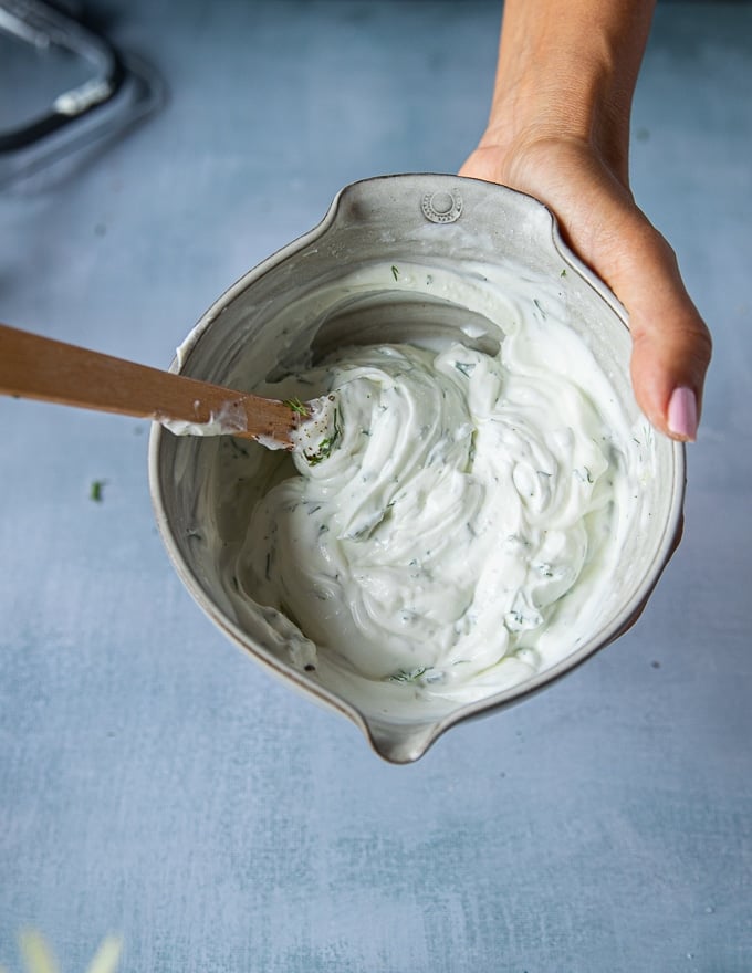 A hand holding a bowl of the finished yogurt sauce