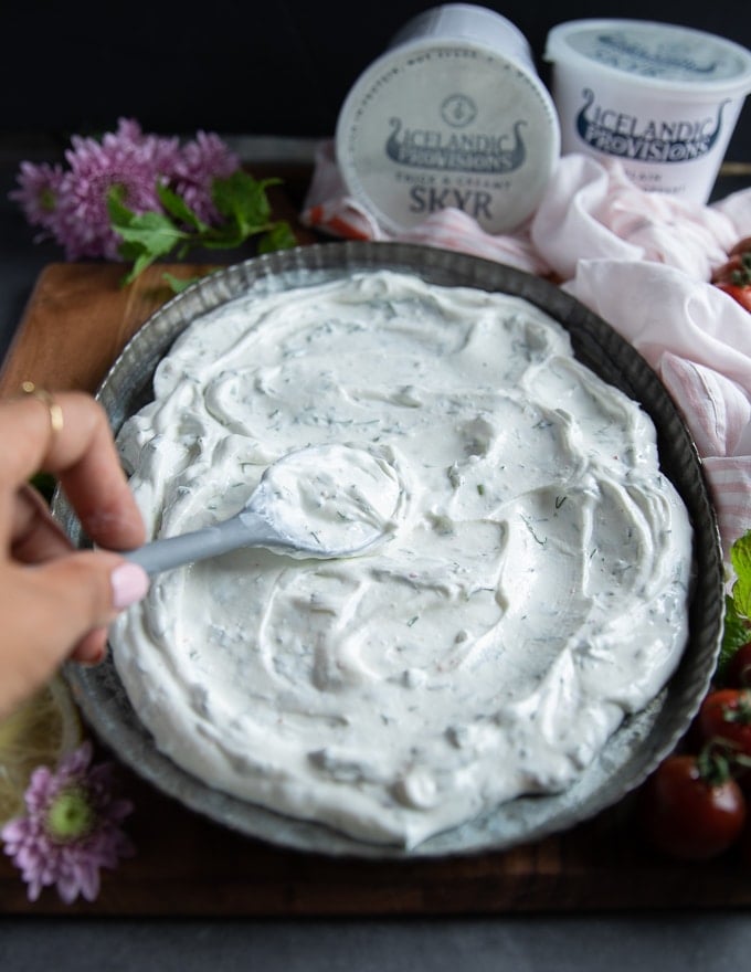 a hand spreading the skyr sauce at the bottom of the plate