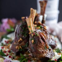 lamb shanks are placed over the skyr sauce and hen garnished with parsley, pine nuts and pomegranate arils