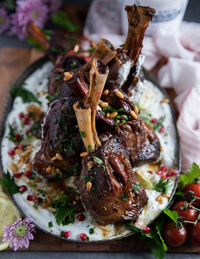 Finished plate of roast lamb shanks recipe over skyr sauce garnished with pomegranate , herbs and pine nuts ready to serve