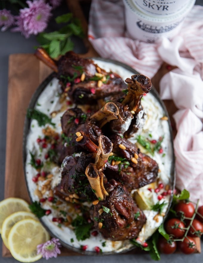 A plate of roast lamb shanks over skyr sauce surrounded by lemon slices