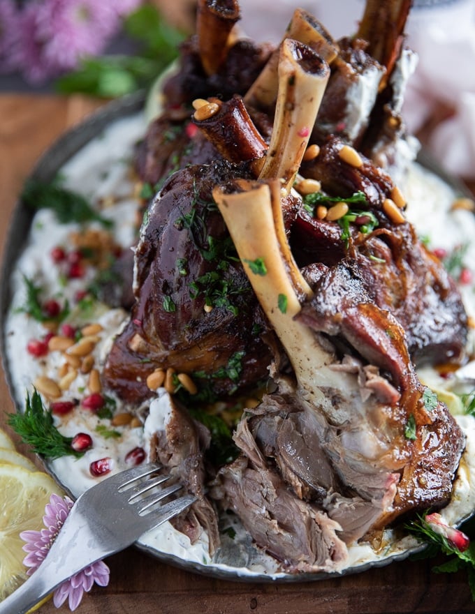 A fork cutting through the cooked lamb shanks showing how soft and juicy the inside is