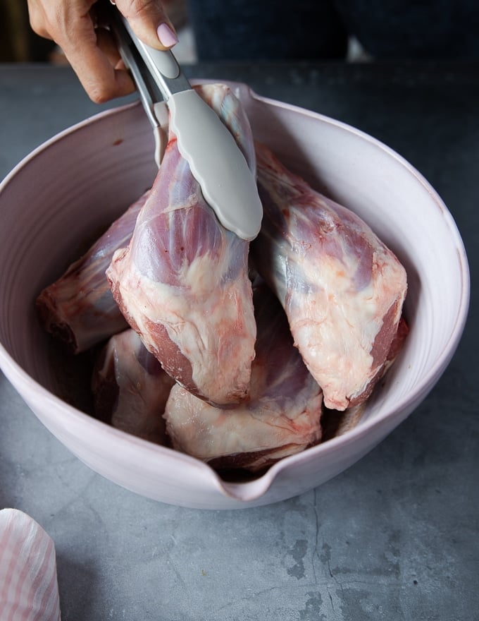 A hand placing the lamb shanks in the bowl of marinade to flavor and toss well