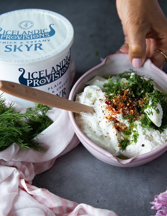 A bowl with skyr added and then seasoning, fresh herbs, lemon juice, garlic and spice ready to make skyr sauce