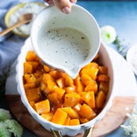 A hand drizzling the basil cream over the fully roasted butternut squash