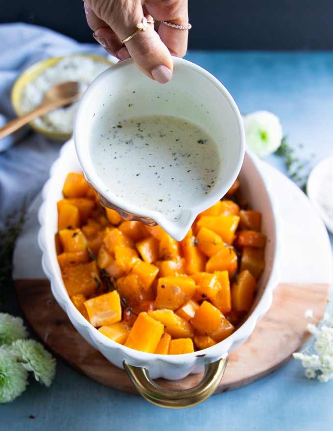 A hand drizzling the basil cream over the fully roasted butternut squash 