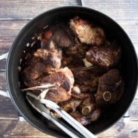 the seared lamb chops going back into the pan with the onions and tomatoes and stock to cook