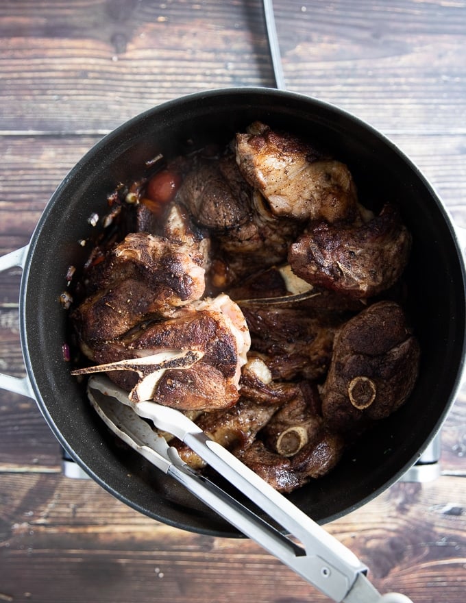 the seared lamb chops going back into the pan with the onions and tomatoes and stock to cook