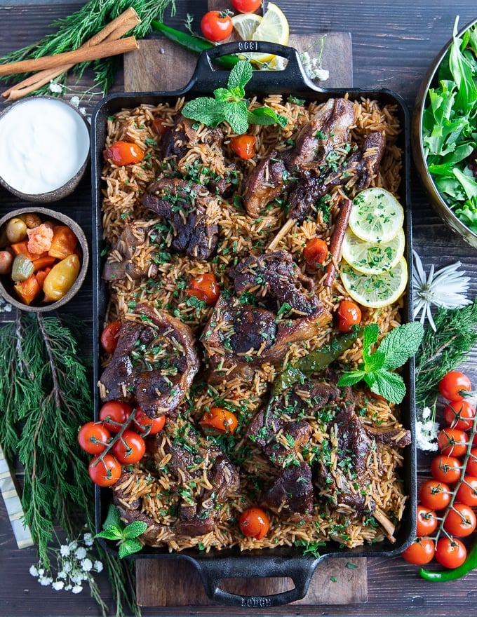 Full plate of cooked lamb shoulder chops, rice and a bowl of salad, some oickles and a bowl of yogurt in the side.