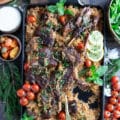 A hand holding off a piece of cooked lamb shoulder chops over the plate of rice and lamb