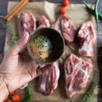 A hand holding a simple lamb seasoning in a bowl made of salt, pepper, oregano and nutmeg