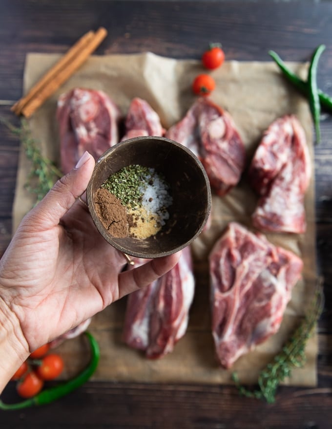 A hand holding a simple lamb seasoning in a bowl made of salt, pepper, oregano and nutmeg 